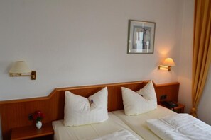 Een hotelkamer met twee bedden, een nachtkastje met een lamp, een ingelijst schilderij aan de muur en een bloemenvaas.