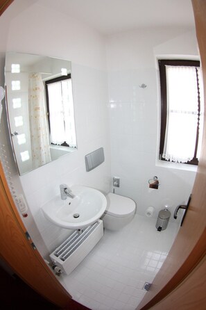 A bathroom with a white sink, a toilet, a mirror, and a window. - Arkaden Hotel (Kelkheim)