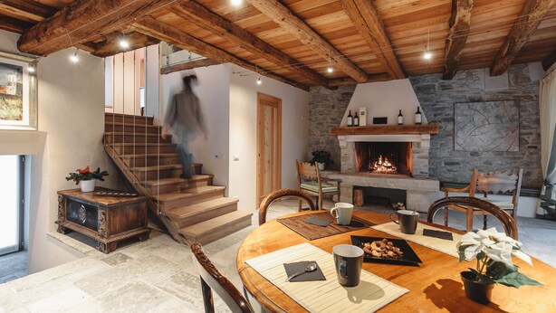 A rustic interior with a stone fireplace, wooden staircase, and a dining area with a round table and chairs. - Il Fontego (Borgo Valbelluna)