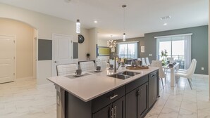Une cuisine moderne dotée d’un grand îlot central, de meubles de rangement aux couleurs sombres et d’un éclairage suspendu.