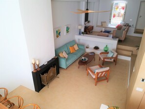 A living room with a sofa, coffee table, and chairs. There is a fireplace with a mantel and a window with bars.