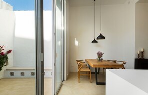A modern dining area with a wooden table and chairs, a black pendant light, and a view through a glass door to an outdoor space.