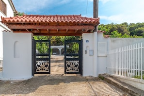 A gated entrance with a tiled roof, a white wall, and a white fence.