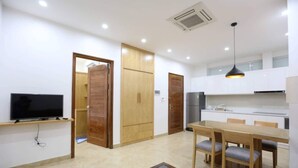 A modern kitchen with white cabinets, a dining table with chairs, a TV on a stand, and a ceiling fan.