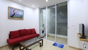 A living room with a red sofa, a glass coffee table, a television on a wooden stand, and a sliding glass door leading to a balcony.