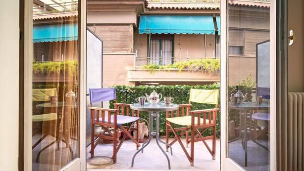 A glass door leading to an outdoor patio with a round table and four chairs, a small table with a teapot, and a blue awning above a balcony. - Kolonaki Hill View Apartment (Athens)