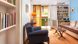 A cozy living room with a blue armchair, a coffee table, and bookshelves filled with books. - Kolonaki Hill View Apartment (Athens)