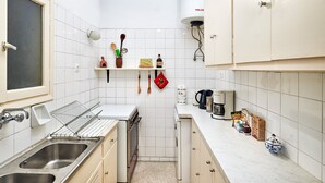 A compact kitchen with white tiles, a stove, a sink, and a countertop with various items. - Kolonaki Hill View Apartment (Athens)