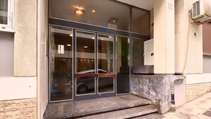 A building entrance with a glass door, steps leading up to it, and a vehicle parked inside. - Kolonaki Hill View Apartment (Athens)