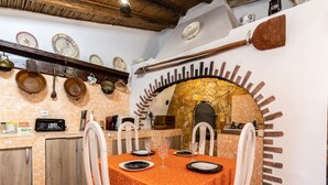 Zona pranzo con tavolo imbandito per quattro persone, forno a pietra e ripiano con stoviglie.