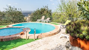 Una piscina circolare con bordo in pietra, circondata da una terrazza con poltrone da relax e una pianta in vaso.