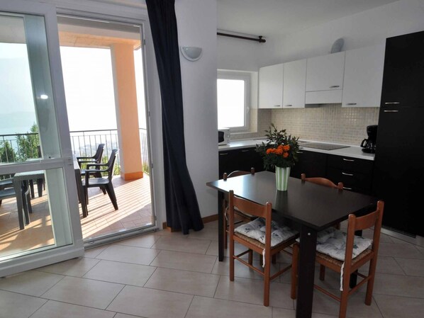 A modern kitchen with white cabinets, a dining table with chairs, a black refrigerator, and a balcony with chairs and a table.