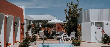 A swimming pool with lounge chairs and umbrellas, surrounded by potted plants and a modern building.