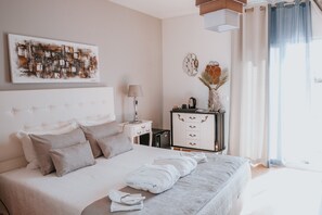 A modern bedroom with a large bed, a bedside table, a lamp, a dresser, and a painting on the wall.