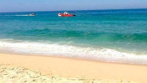 Een strand met helder turquoise water, een zandstrand en twee boten in de verte.