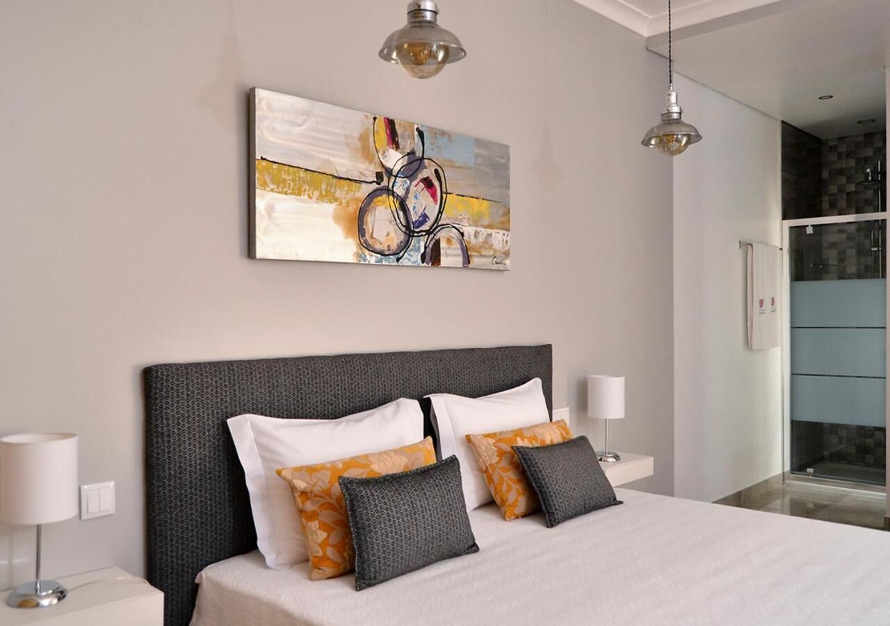A modern bedroom with a large bed, two bedside lamps, a wall-mounted abstract painting, and a glass shower area.