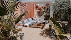 Een zonnig terras met een hangmat, comfortabele zitplaatsen en planten in potten.