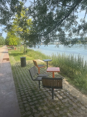 Un parco lungo il fiume con panchine, un percorso pedonale lastricato e vista sull'acqua.