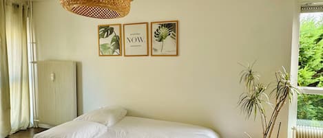 A bedroom with a large bed, a woven light fixture, and framed botanical prints on the wall.