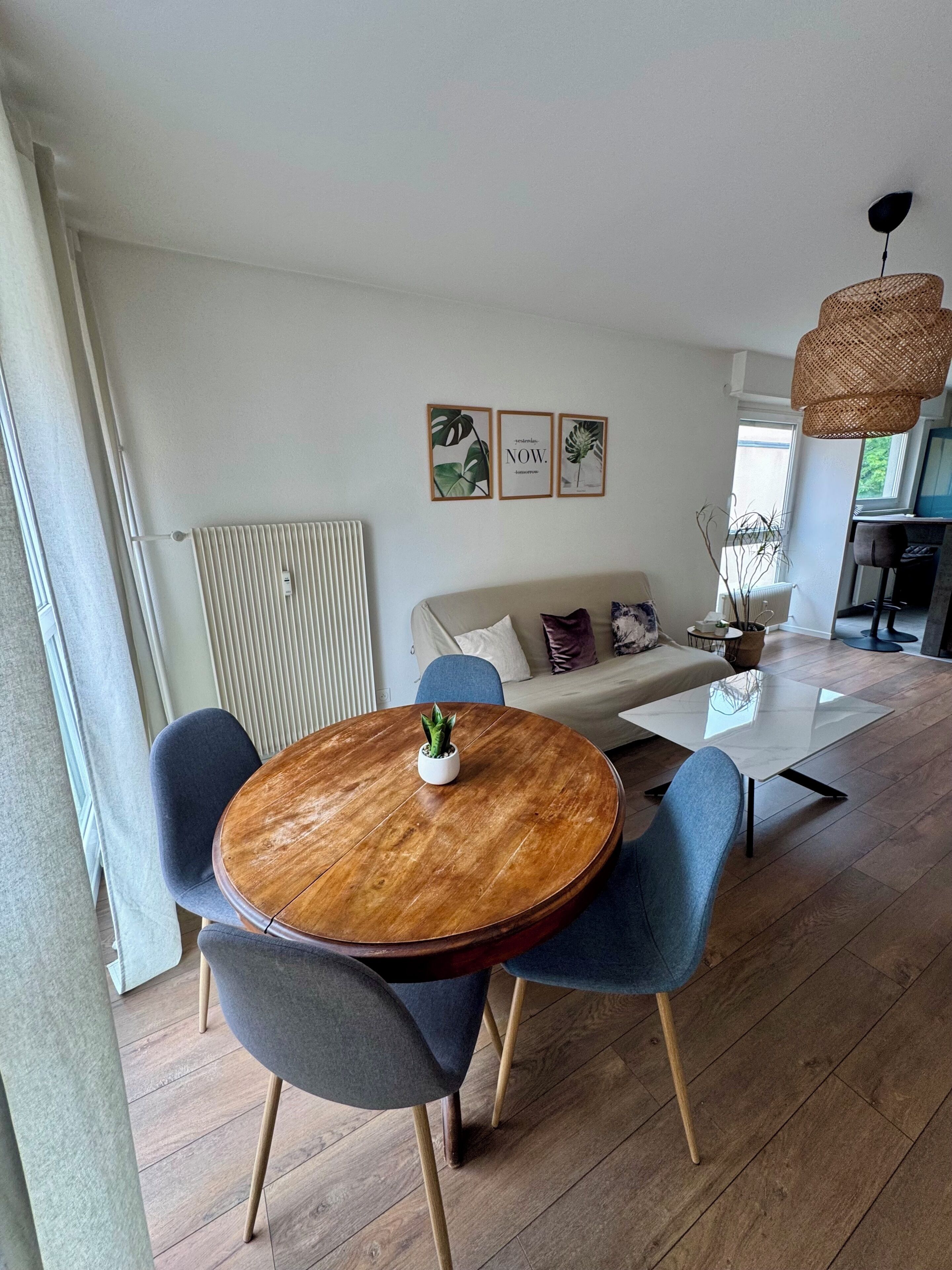 Una sala de estar moderna con una mesa redonda de madera, sillas azules, un sofá y una lámpara colgante.