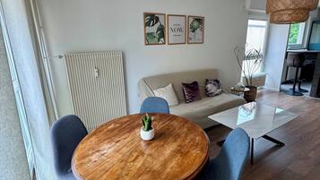 Una sala de estar moderna con una mesa redonda de madera, sillas azules, un sofá y una lámpara colgante.