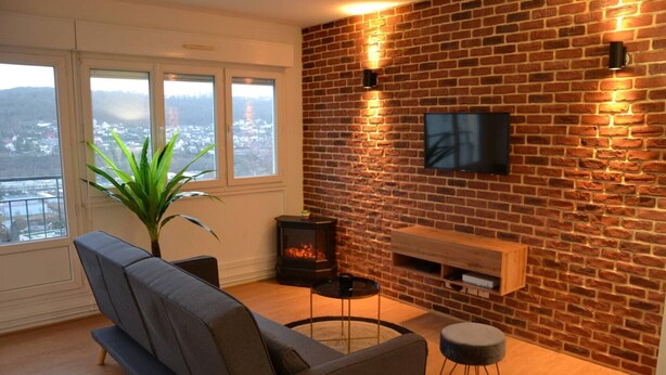 Uma sala de estar moderna com parede de tijolos, televisão de tela plana, sofá, mesa pequena, planta e lareira.