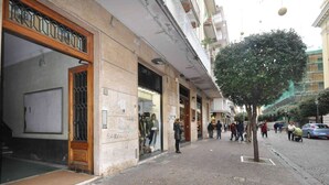Una calle adoquinada con comercios, una acera arbolada y peatones.