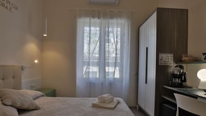 Habitación de hotel con cama, escritorio con cafetera, armario y ventana con cortinas traslúcidas.