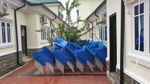 Varias sillas azules apiladas frente a un edificio con detalles blancos y unidades de aire acondicionado.