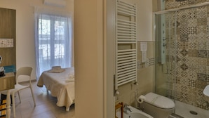 Habitación de hotel con una cama, un escritorio, una silla, un baño con ducha, lavamanos e inodoro.