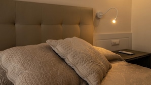 Un dormitorio con cabecera capitonada, lámpara de noche y cama con colcha acolchada.