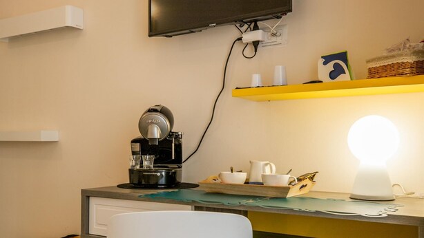Un espace de travail compact équipé d’une machine à café, d’un téléviseur à écran plat et d’une lampe de bureau lumineuse.
