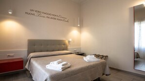 Ein modernes Hotelzimmer mit einem großen Bett, einem Nachttisch, einem roten Schrank und einem Spiegel an der Wand.