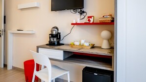 Ein kompakter Wohnbereich mit Küchenzeile, einem an der Wand befestigten Fernseher, einer kleinen Sitzecke mit einem Sessel und einem Mülleimer.