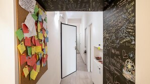Ein Flur mit einer Korkwand voller bunter Notizen, einer Tür zu einem anderen Raum und einer Wand mit Kreideanschriften.