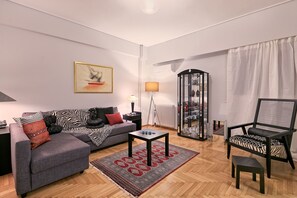 Una sala de estar moderna con un sofá gris, un plaid blanco y negro, una mesita de centro pequeña, un sillón negro y un aparador de vidrio con objetos decorativos.