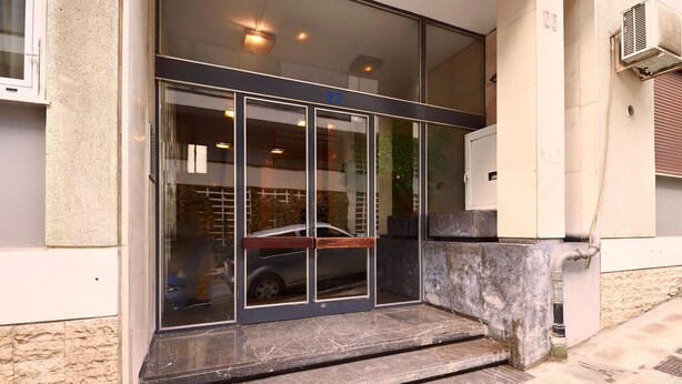 A building entrance with a glass door, steps leading up to it, and a vehicle parked inside.