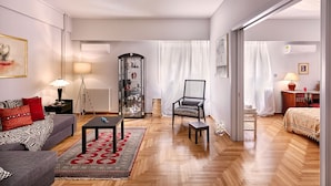 A modern living room with a grey sofa, a black coffee table, and a patterned rug. There is a glass cabinet with decorative items and a black chair.