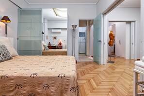 A modern bedroom with a large bed, a glass partition, a dining area, and a hallway leading to a bathroom. - Central Kolonaki Apartment (Athens)