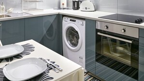 A modern kitchen with a built-in washing machine, oven, and a dining area with a table set for two.