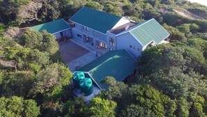 An aerial view of a coastal property with a large house featuring a green roof, surrounded by dense vegetation and a beach in the background. - Kangela 7 (Ponta d'Ouro)