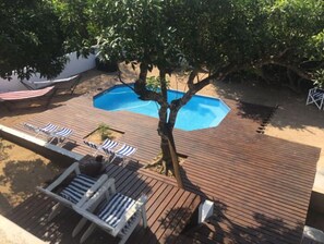 Eine Holzterrasse mit Swimmingpool, Liegestühlen und einer Hängematte.