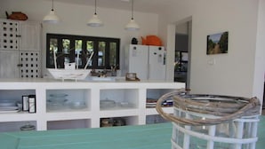 A kitchen with white cabinets, a large window, and a hanging light fixture. - Kangela 7 (Ponta d'Ouro)