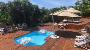 A wooden deck with a swimming pool, lounge chairs, and a shaded area with an umbrella. - Kangela 7 (Ponta d'Ouro)
