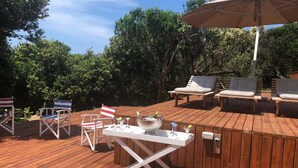 An outdoor deck with wooden flooring, a white table with a bowl of drinks, and lounge chairs. - Kangela 7 (Ponta d'Ouro)