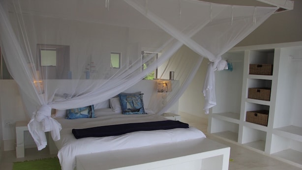 A bedroom with a canopy bed, white walls, and built-in shelving with baskets. - Kangela 7 (Ponta d'Ouro)