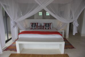 Ein geräumiges Schlafzimmer mit einem großen Bett, weißen Vorhängen und Kissen im Seestil.