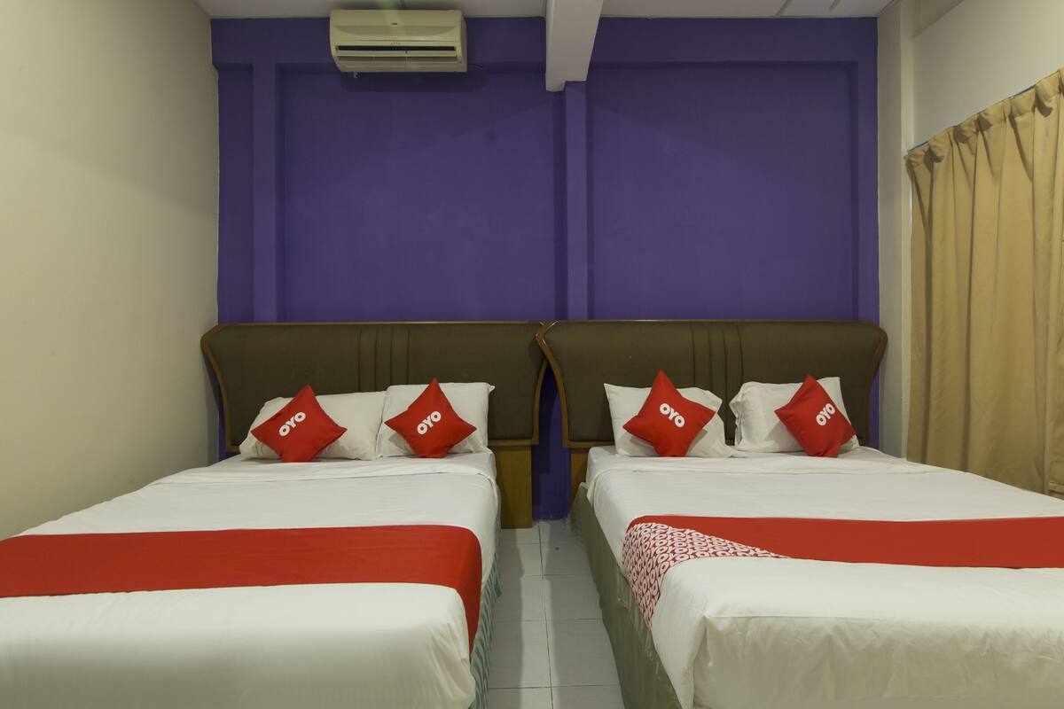 A hotel room with two beds, purple walls, and a beige curtain.