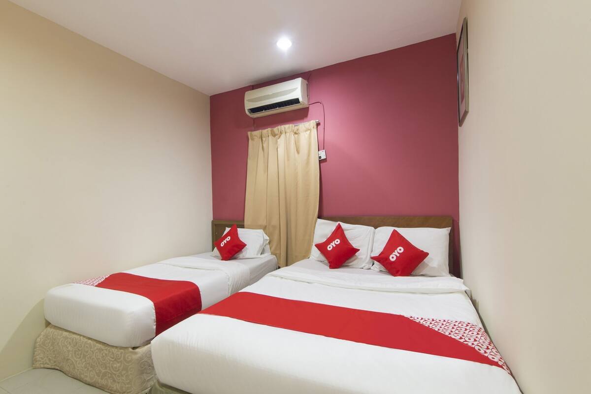 A hotel room with two beds, red and white bedding, an air conditioning unit, and a curtain.