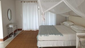 A bedroom with a bed under a canopy, a bedside table, a mirror, and a window with curtains. - Kangela 11 (Ponta d'Ouro)